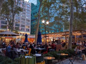 Kerst in Bryant Park: kale bomen, glazen gebouwen, ijzeren tafeltjes en stoelen, warme sfeerverlichting, kerststalletjes gemaakt van glas