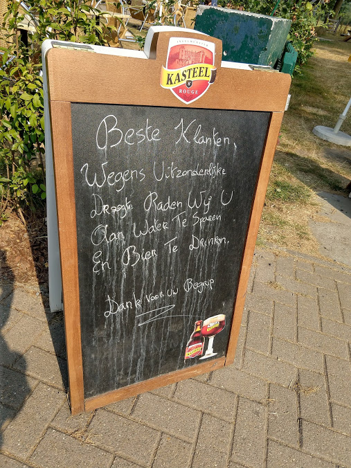 Bord "Beste klanten, wegens uitzonderlijke droogte raden wij u aan water te sparen en bier te drinken. Dank voor uw begrip."