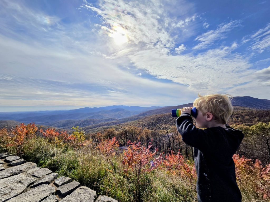 jongen kijkt met verrekijker uit over berglandschap in de herfst
