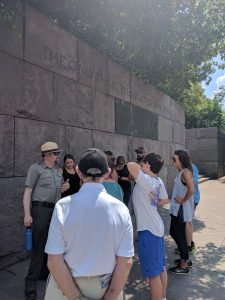 Ranger staat met typische groene kledij, hoed en zonnebril voor muur met citaat FDR uitleg te geven, omringd door bezoekers